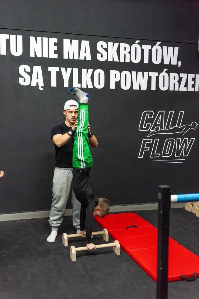 Trener asekuruje podopiecznego podczas ćwiczenia na poręczach