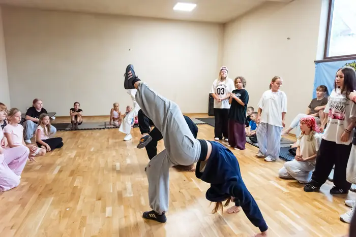 Pokaz breakdance na sali tanecznej, grupa ogląda z boku